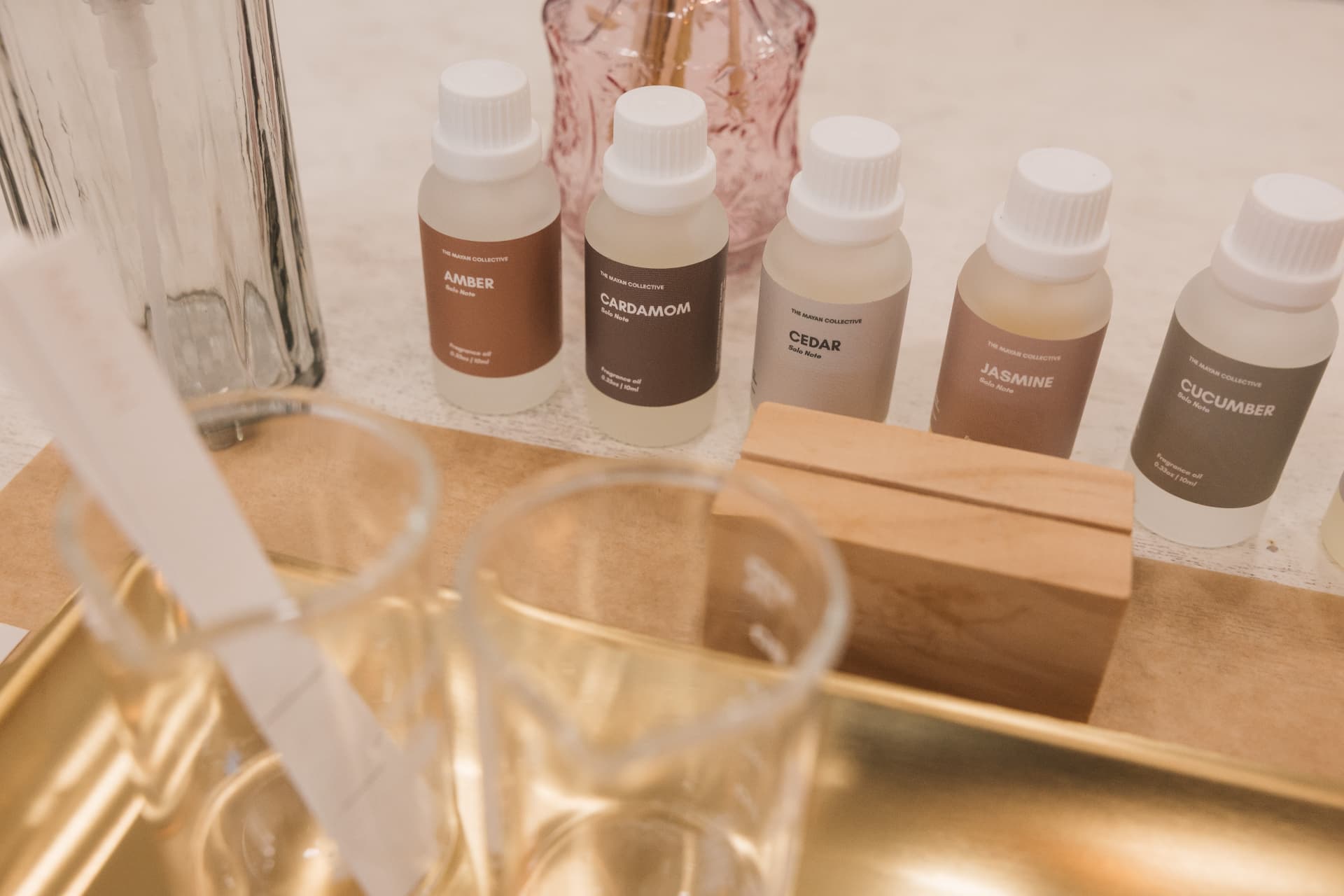 Labeled fragrance oils lined up beside blending beakers on a gold tray